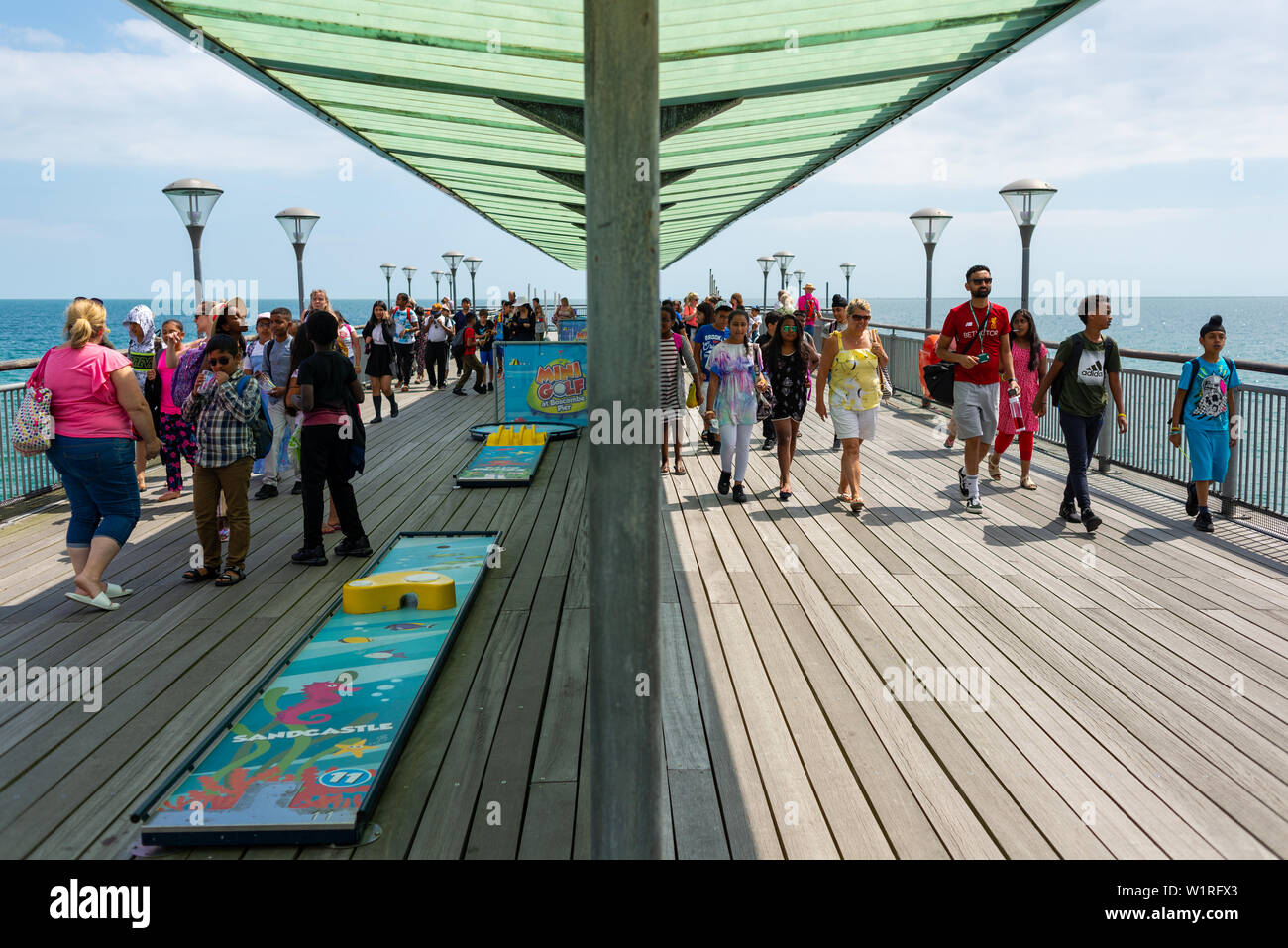 Une partie d'élèves parmi les gens sur la jetée victorienne restaurée à Boscombe, Dorset, England, UK. Les gens qui marchent dans des directions opposées. Banque D'Images
