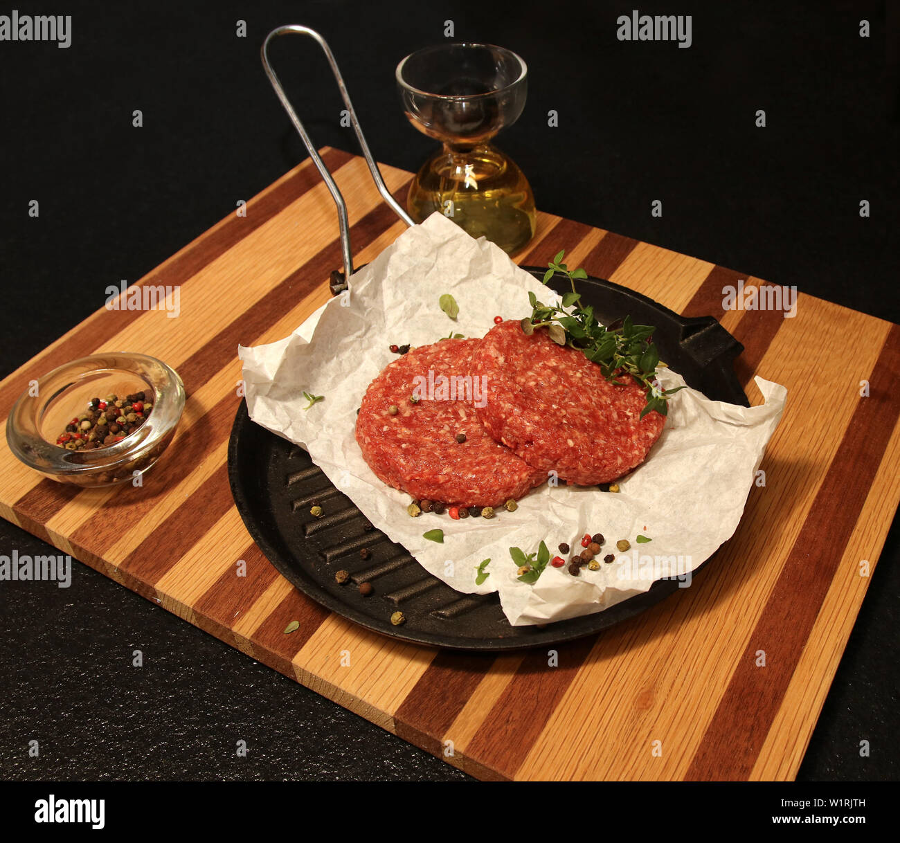 Deux hamburgers de bœuf sur une poêle sur une planche en bois avec un fond noir. Banque D'Images