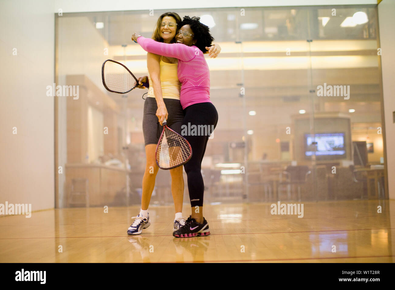 Two smiling women hugging en étant debout sur un court de racquetball. Banque D'Images