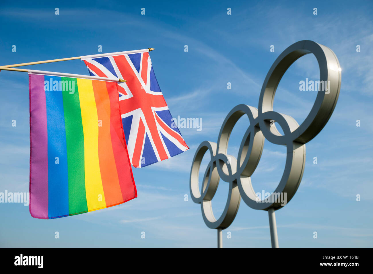 Londres - 4 mai 2019 : Une couleur arc-en-ciel du drapeau de la gay pride se tient avec un drapeau japonais en face d'Anneaux olympiques contre ciel bleu. Banque D'Images