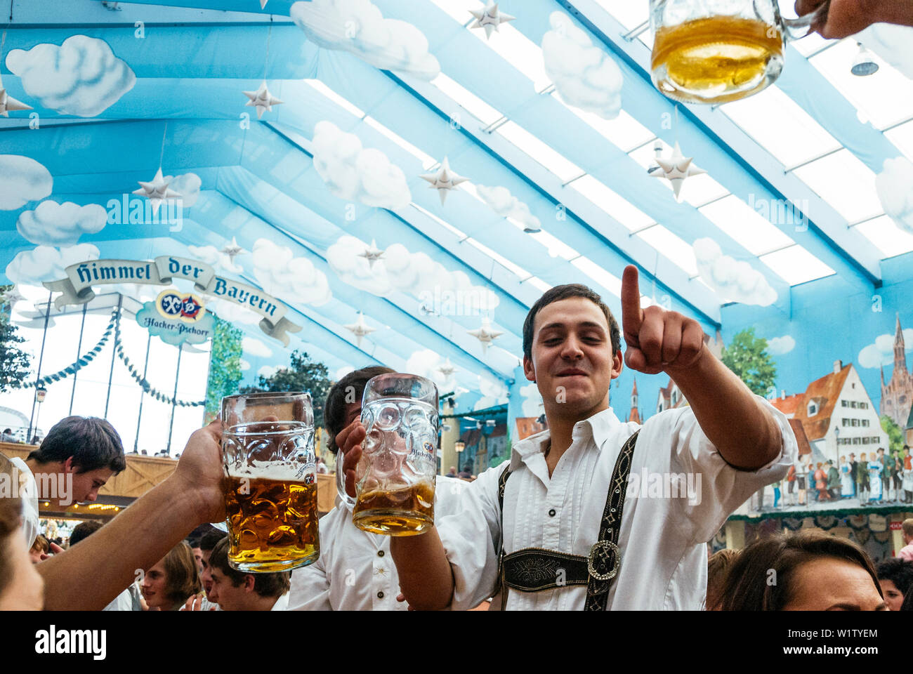 Jeune homme en pantalon de cuir debout sur les bancs de la bière Oktoberfest célébrer dans la tente à bière Banque D'Images