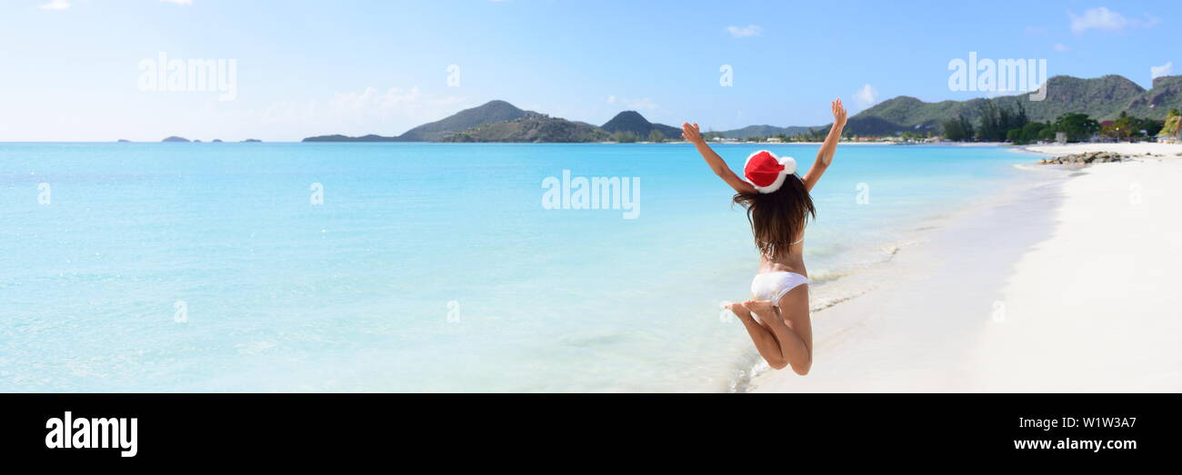 Woman with arms outstretched jumping at beach. Vue arrière de femelle est wearing Santa hat et bikini. L'insouciante est bénéficiant de Noël locations aux beaux jours. Banque D'Images