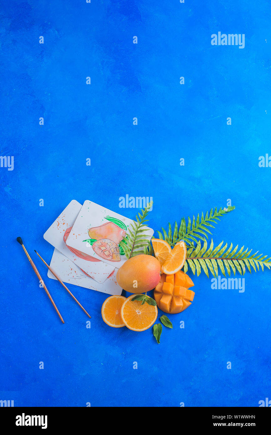 Les mangues jaunes et oranges avec des feuilles tropicales et croquis à l'aquarelle sur fond bleu vif avec copie espace. Couleurs complémentaires art photographe Banque D'Images