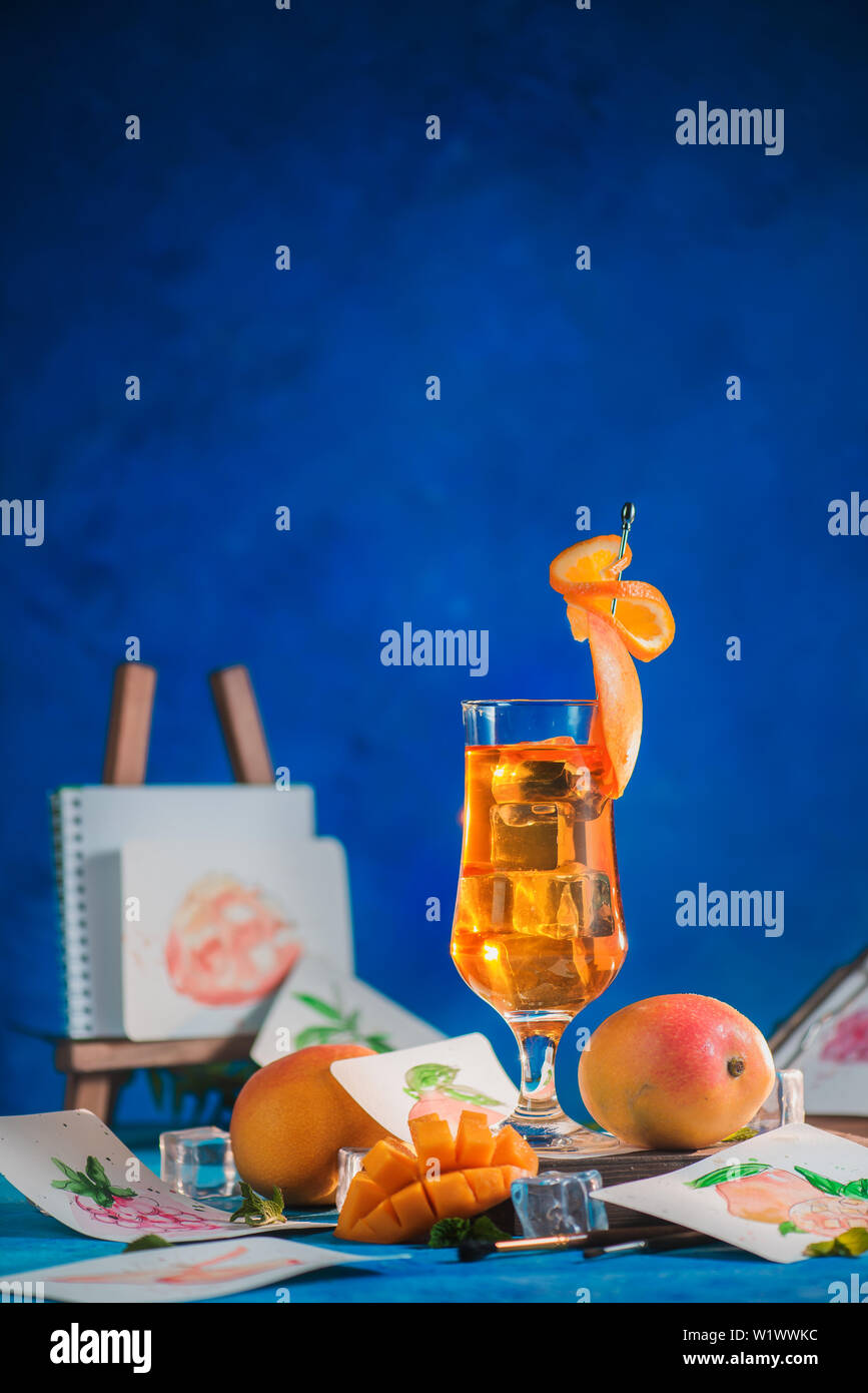 Des boissons d'été dans des grands verres avec des croquis dans un milieu de travail de l'artiste. mangue et thé glacé orange sur un fond bleu avec copie espace Banque D'Images