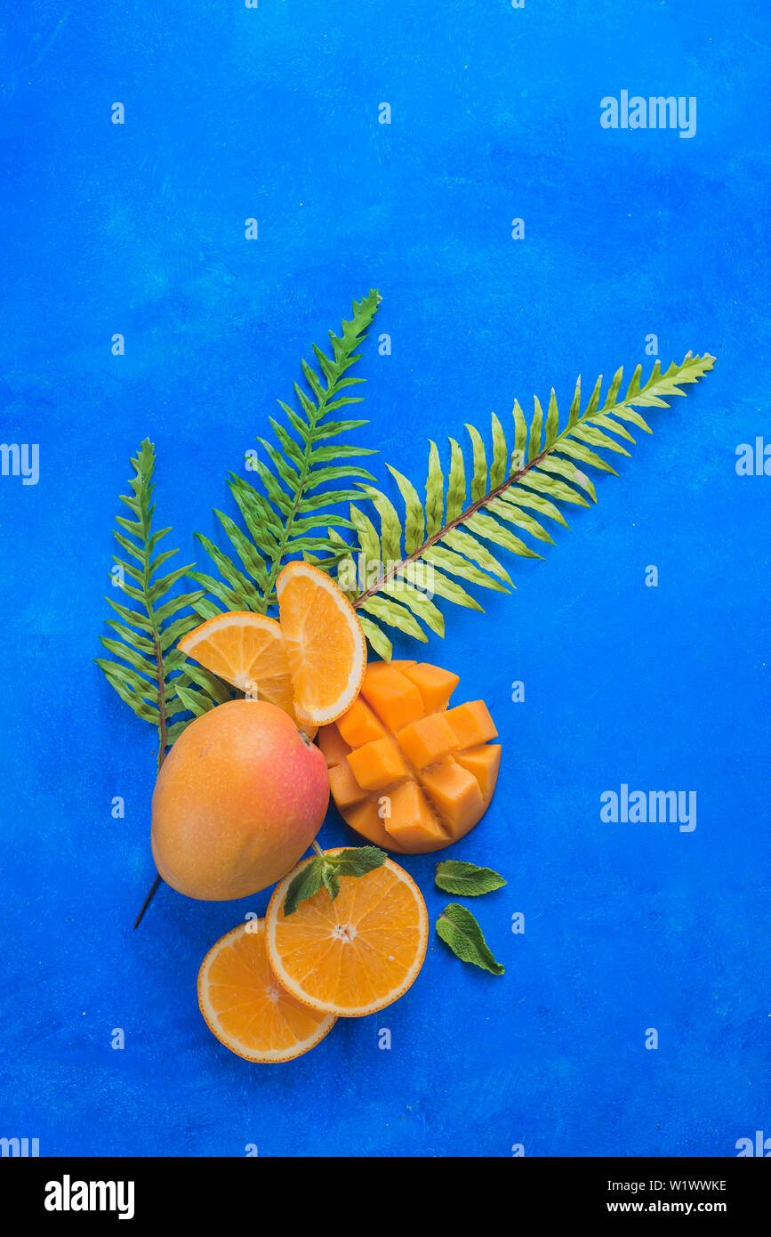 Fruits exotiques sur fond bleu vif avec copie espace. Mangue et orange avec les feuilles tropicales mise à plat. Banque D'Images