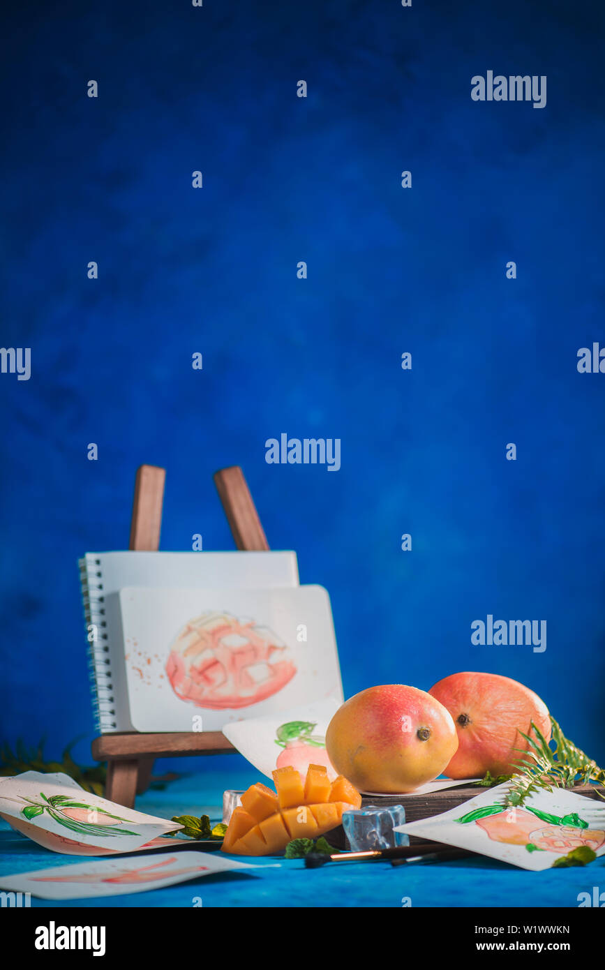 Fruits exotiques avec des croquis dans un milieu de travail de l'artiste. Mangue et orange sur un fond bleu avec copie espace Banque D'Images