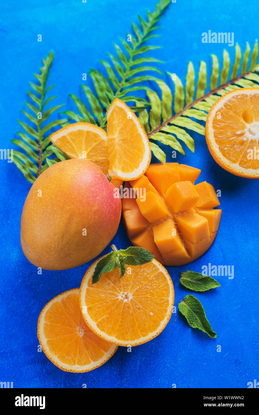 Les mangues, oranges et jaunes sur fond bleu vif avec copie espace. Couleurs complémentaires still life. Les feuilles tropicales Banque D'Images