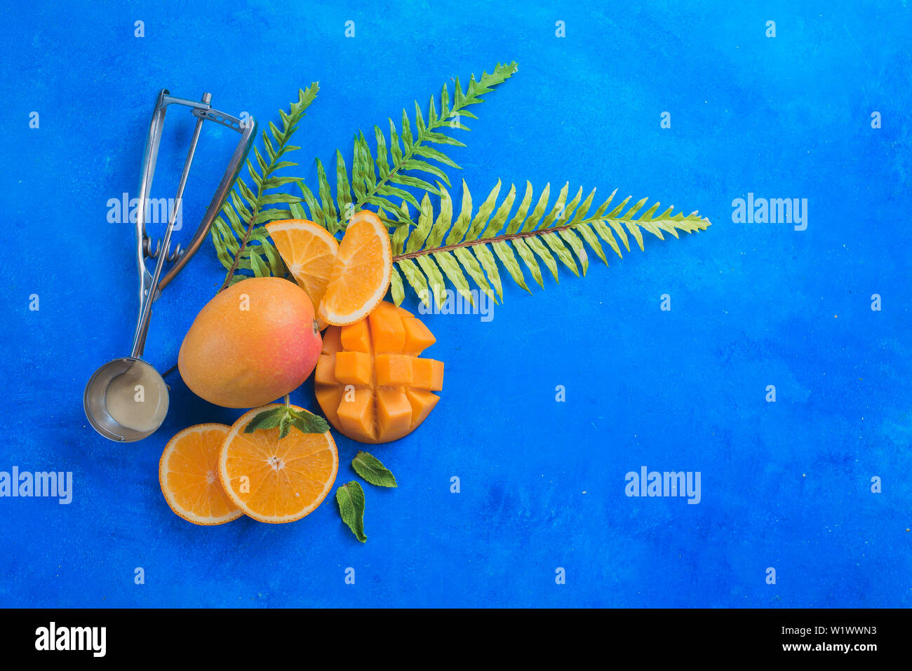 Cuillère de crème glacée aux fruits exotiques, mangues et oranges sur fond bleu vif avec copie espace. Télévision ingrédients lay. Banque D'Images