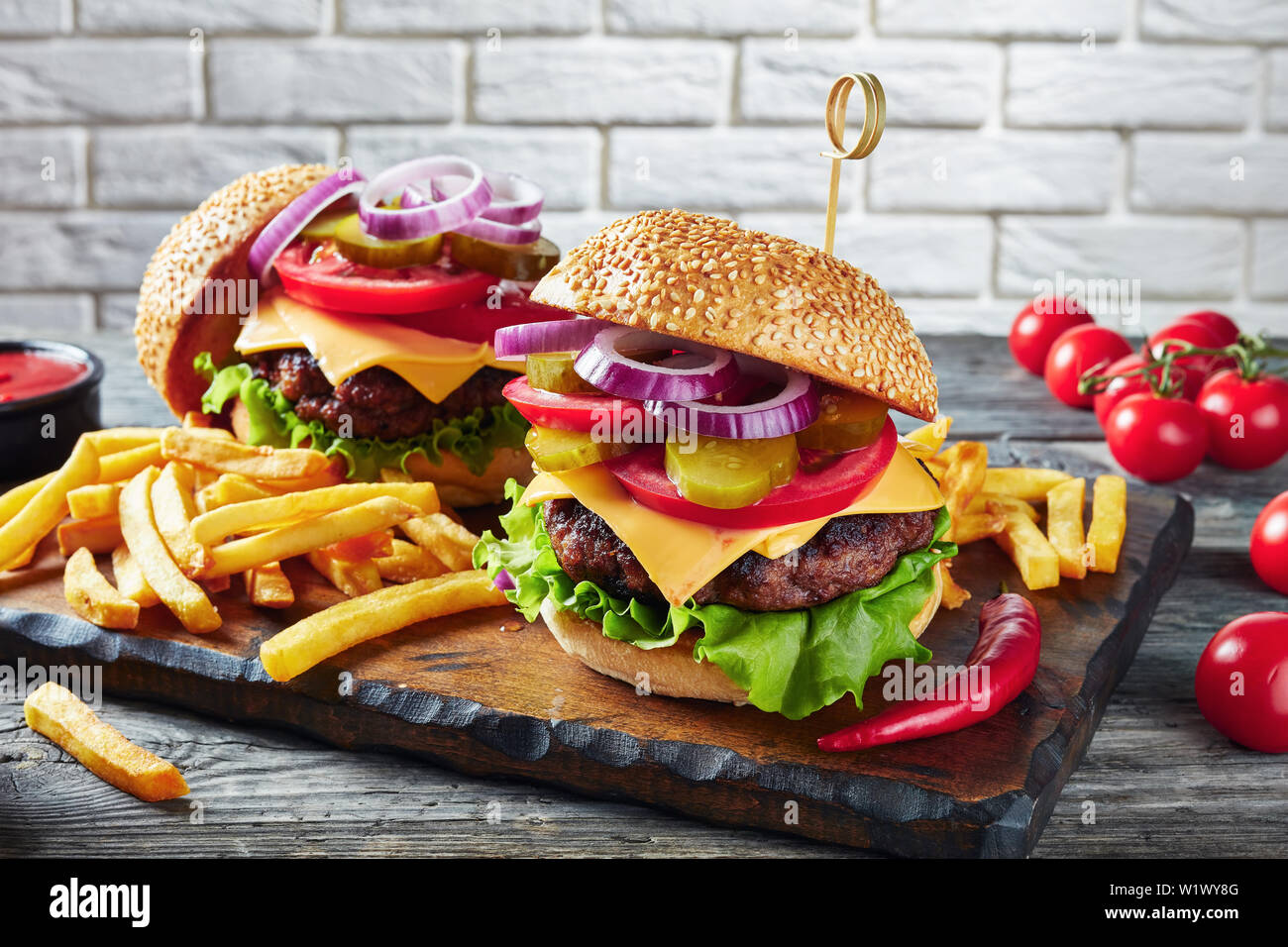 Des hamburgers avec fromage cheddar, petits pains fraîchement cuits, des burgers de bœuf frit, de cornichons, de la laitue, ketchup, moutarde, oignons, tomates et frites sur Banque D'Images