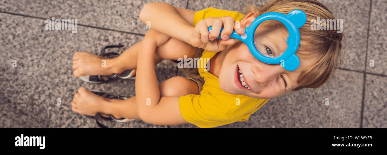 Garçon est assis sur le sol et regarde dans une loupe BANNER, format long Banque D'Images