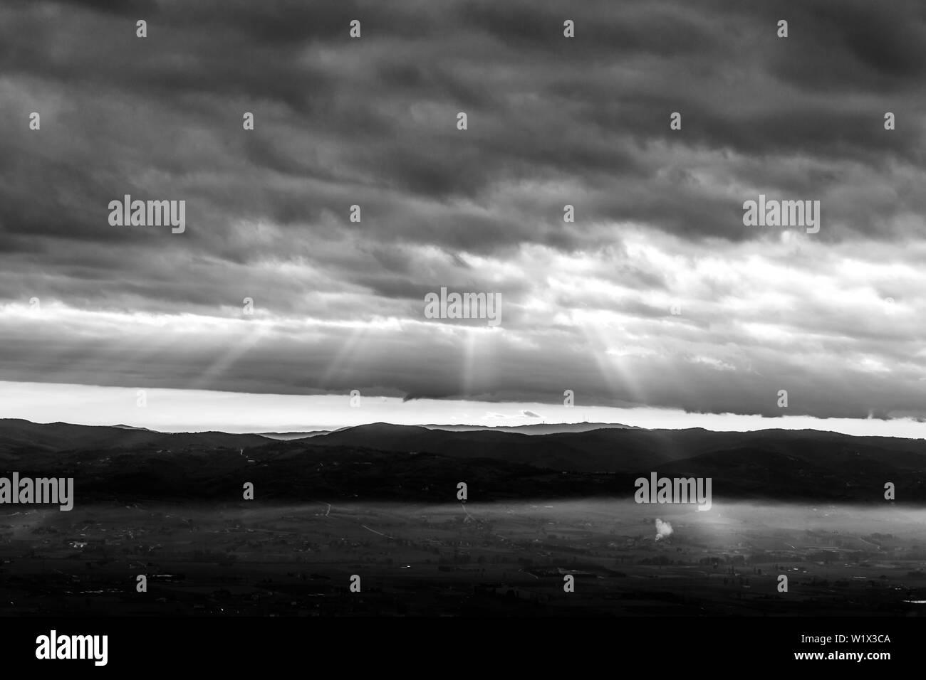 Les rayons du soleil en descendant de quelques nuages sur une vallée plantée par le brouillard, illuminant une partie de celui-ci Banque D'Images