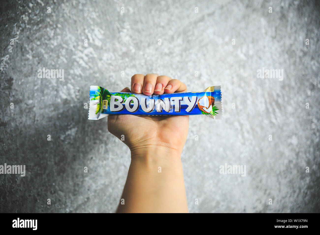 Chocolat Bounty tenant dans la main sur le fond blanc et gris. Banque D'Images