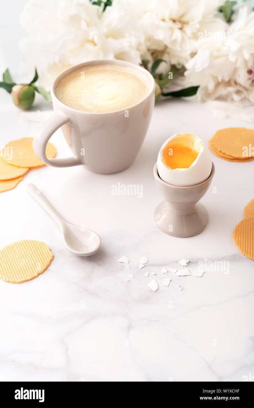 Oeufs à la coque avec liquide jaune orange en céramique egg cup, tasse de café avec cuillère en céramique mince et croustillante et les croustilles de maïs sur fond de belle wh Banque D'Images