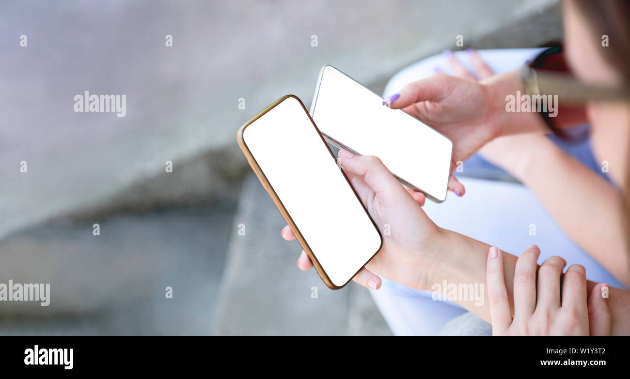 Deux filles holding mobile smart phone à côté de l'autre fond écran blanc maquette partage à l'aide de découpage ou de travail vierge smartphones à sur Banque D'Images