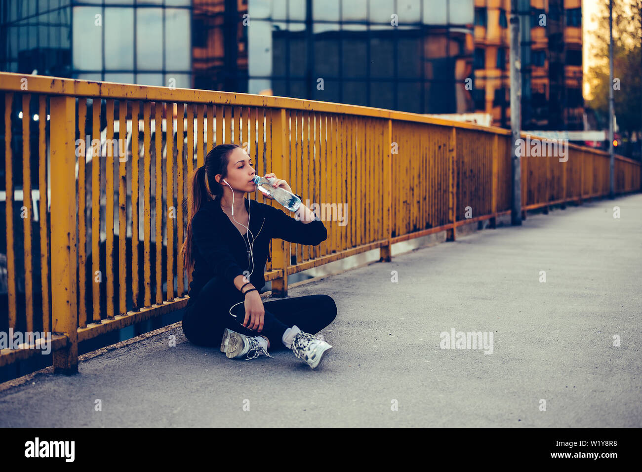 Coureuse assis sur le pont et l'eau potable à partir d'une bouteille. Femme de remise en forme en faisant une pause après l'exécution de l'entraînement. Banque D'Images