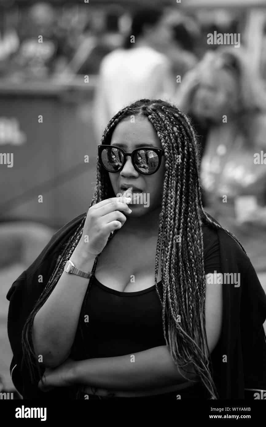 Image Monochrome de jeune femme noire d'appliquer le baume de lèvre at an outdoor summer music festival Banque D'Images