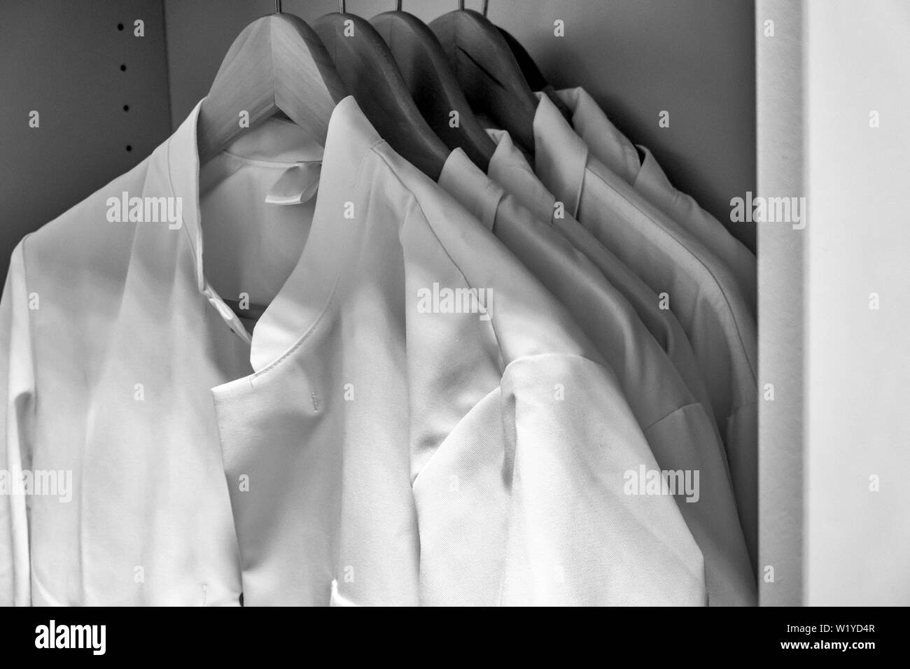 Des blouses blanches sur les cintres en bois suspendus dans l'armoire d'un laboratoire, noir et blanc, P.C. Banque D'Images