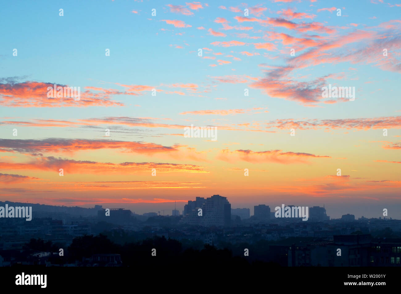 Cityscape tôt le matin : rose et orange nuages sur un ciel bleu à l'aube juste avant le lever du soleil sur la ville endormie background Banque D'Images