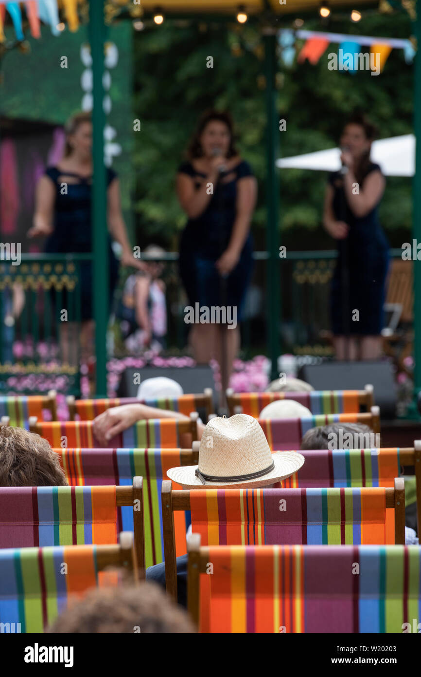 Les gens assis dans des chaises longues à regarder une femme vintage le boogie-woogie groupe chantant dans le kiosque à RHS Hampton Court Flower Show 2019. Surrey, UK Banque D'Images