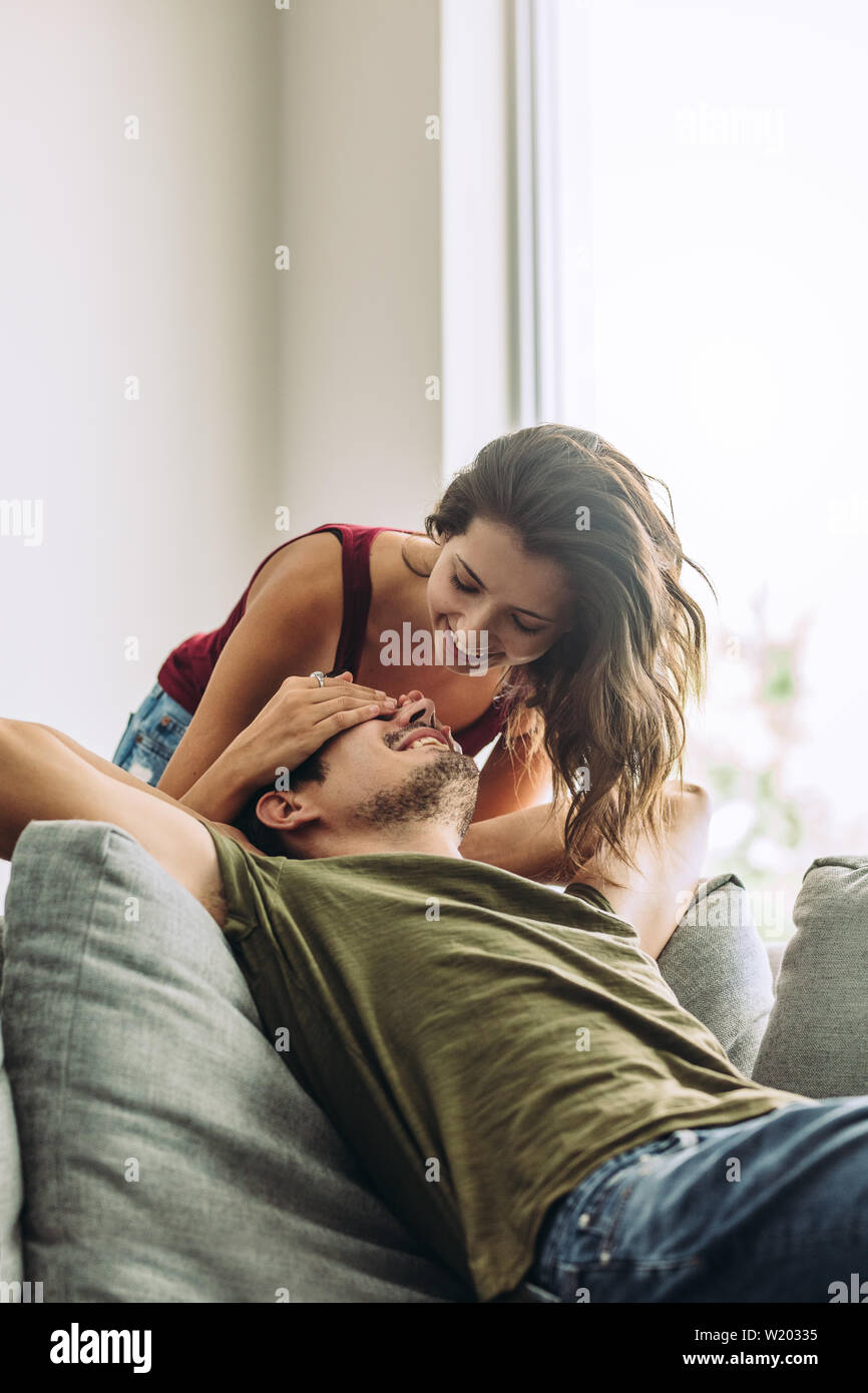 Jeune femme étonnant homme assis dans le salon à la maison. Female couvrant les yeux de son petit ami. Banque D'Images