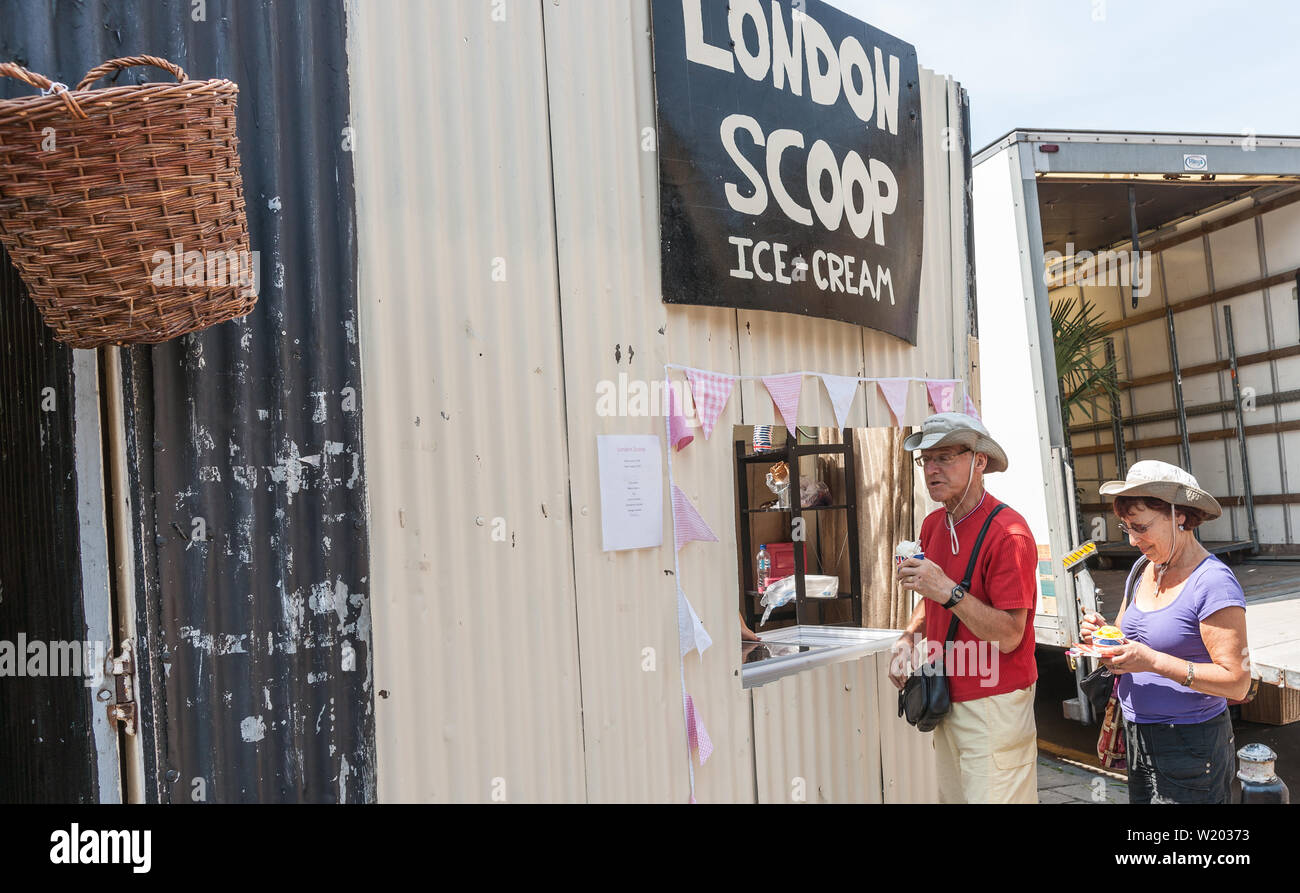 Londres, Angleterre - le 14 juillet 2013 ; Couple dans l'achat de chapeaux de glace openng dans fenêtre mur en tôle ondulée avec signe au-dessus de Londres Scoop. Banque D'Images