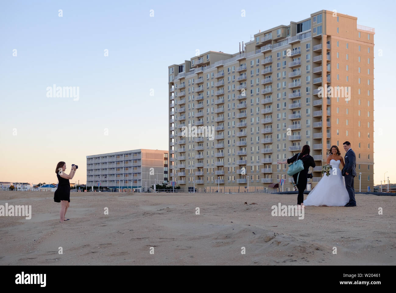 Un photographe de mariage et son adjointe nouvellement mariés posent au coucher du soleil sur le sable au large de la promenade de Virginia Beach, en Virginie. Banque D'Images