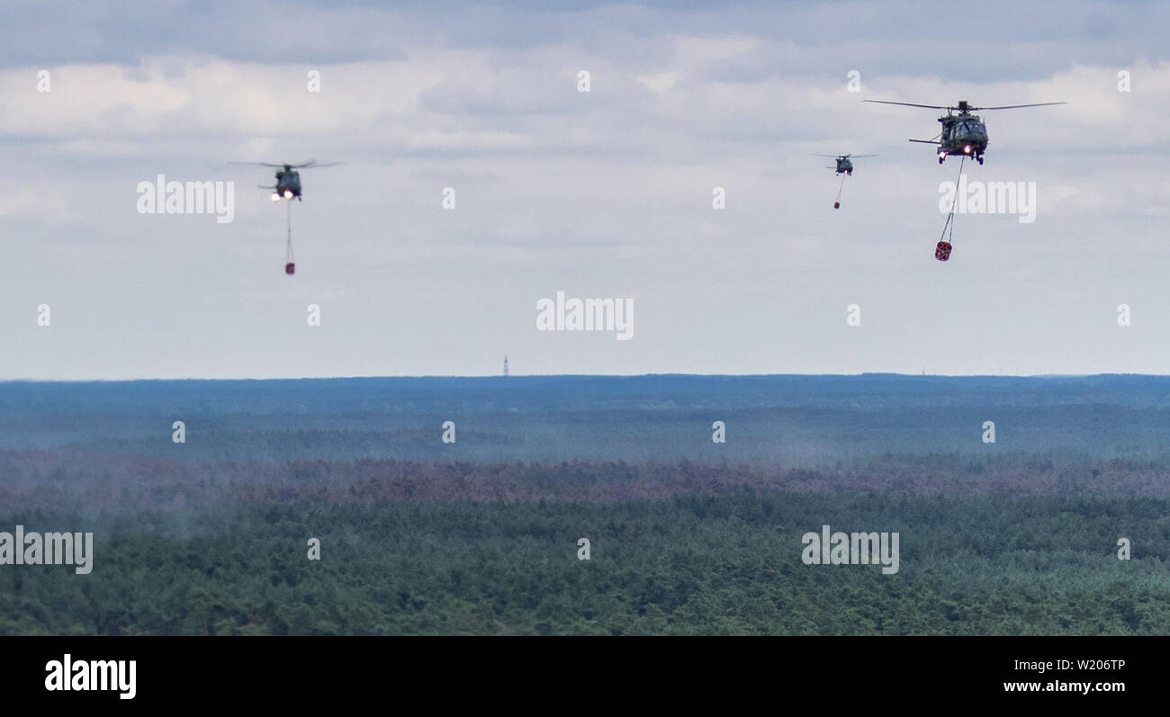 Alt Jabel, Allemagne. Le 04 juillet, 2019. Trois hélicoptères de la Bundeswehr NH90 type avec des réservoirs d'eau d'extinction survoler une forêt près de Alt Jabel et de décharge sur l'eau d'extinction incendie (taches isolées Vue aérienne d'un hélicoptère). La situation dans la zone d'incendie de forêt sur une ancienne zone d'entraînement militaire près de Lübtheen en Mecklembourg-Poméranie-Occidentale a diminué légèrement pour la première fois depuis le début de l'incendie. Les premiers habitants ont été en mesure de retourner dans leurs maisons qui avait été autorisé à titre de précaution. Credit : Jens Büttner/dpa-Zentralbild/dpa/Alamy Live News Banque D'Images