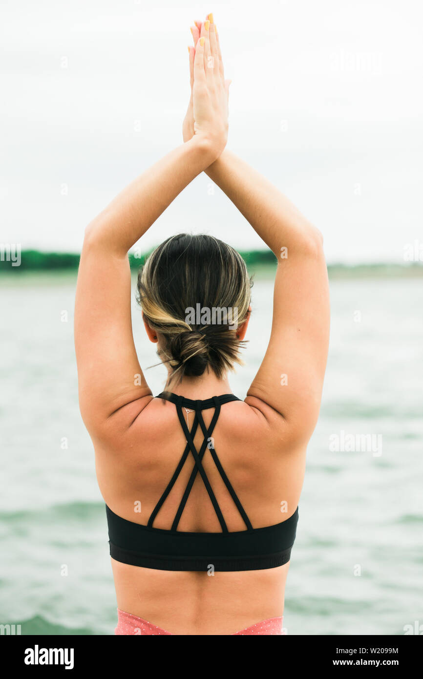 Jeune fille asiatique faisant du yoga en plein air sur le quai près du lac. elle porte un haut noir et des jambières rouges. Banque D'Images