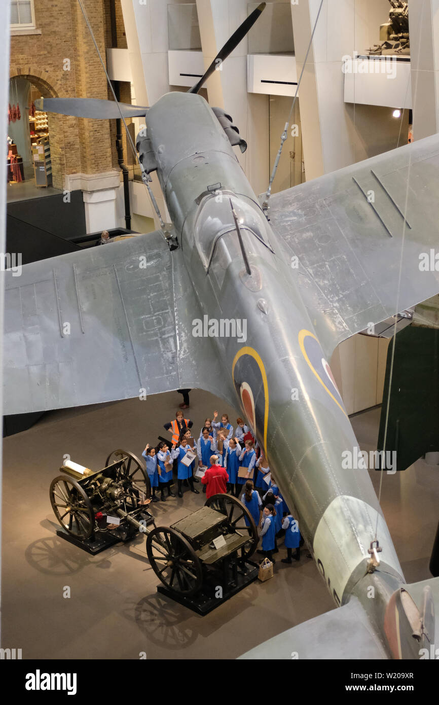 La classe de l'école se réunit sous le Spitfire de la seconde Guerre mondiale pour en apprendre plus sur la seconde Guerre mondiale à l'Imperial War Museum, à Londres. Banque D'Images