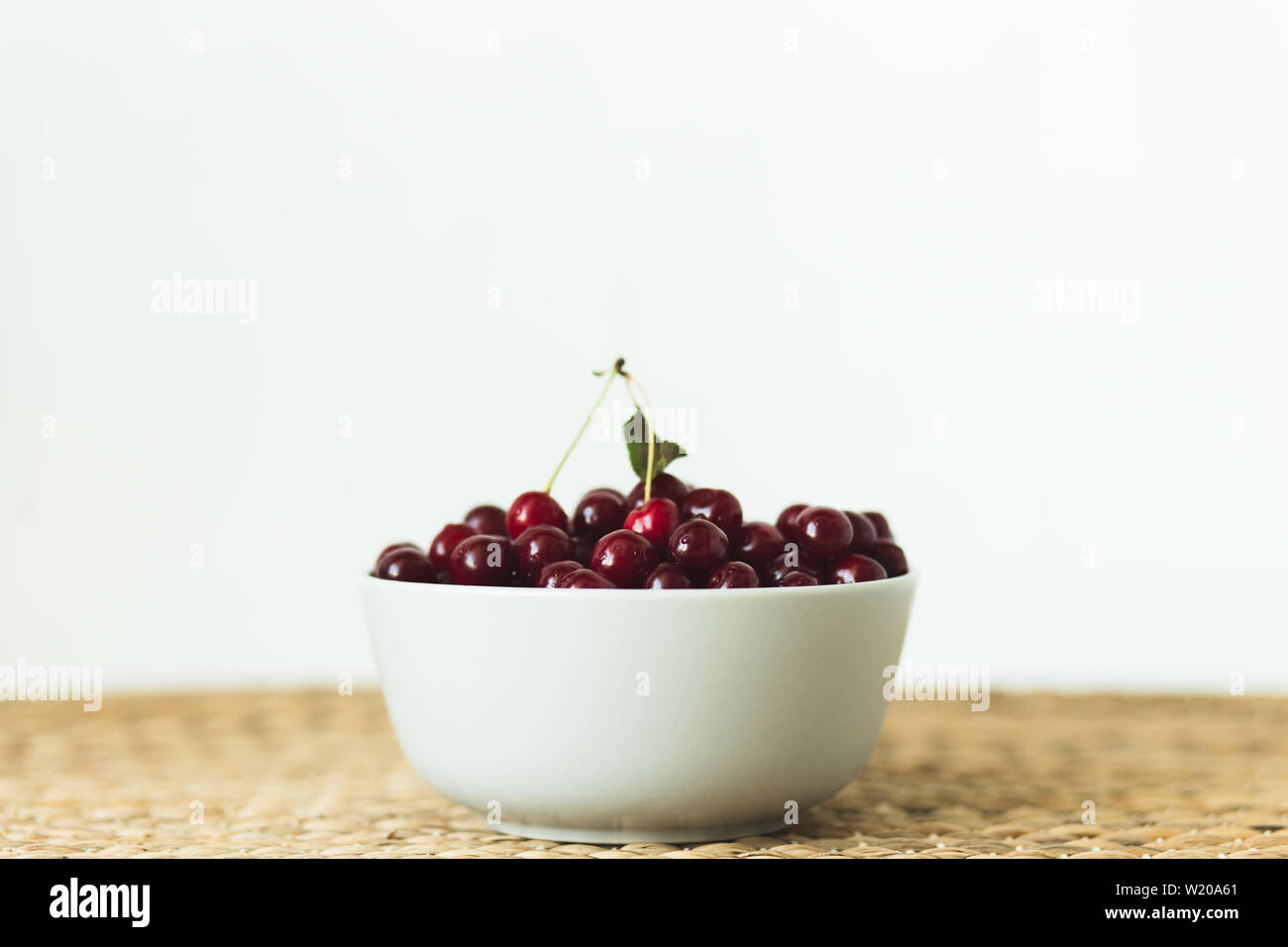 Une assiette pleine de cerises fraîches sur une serviette en osier naturel de fruits de saison. Banque D'Images