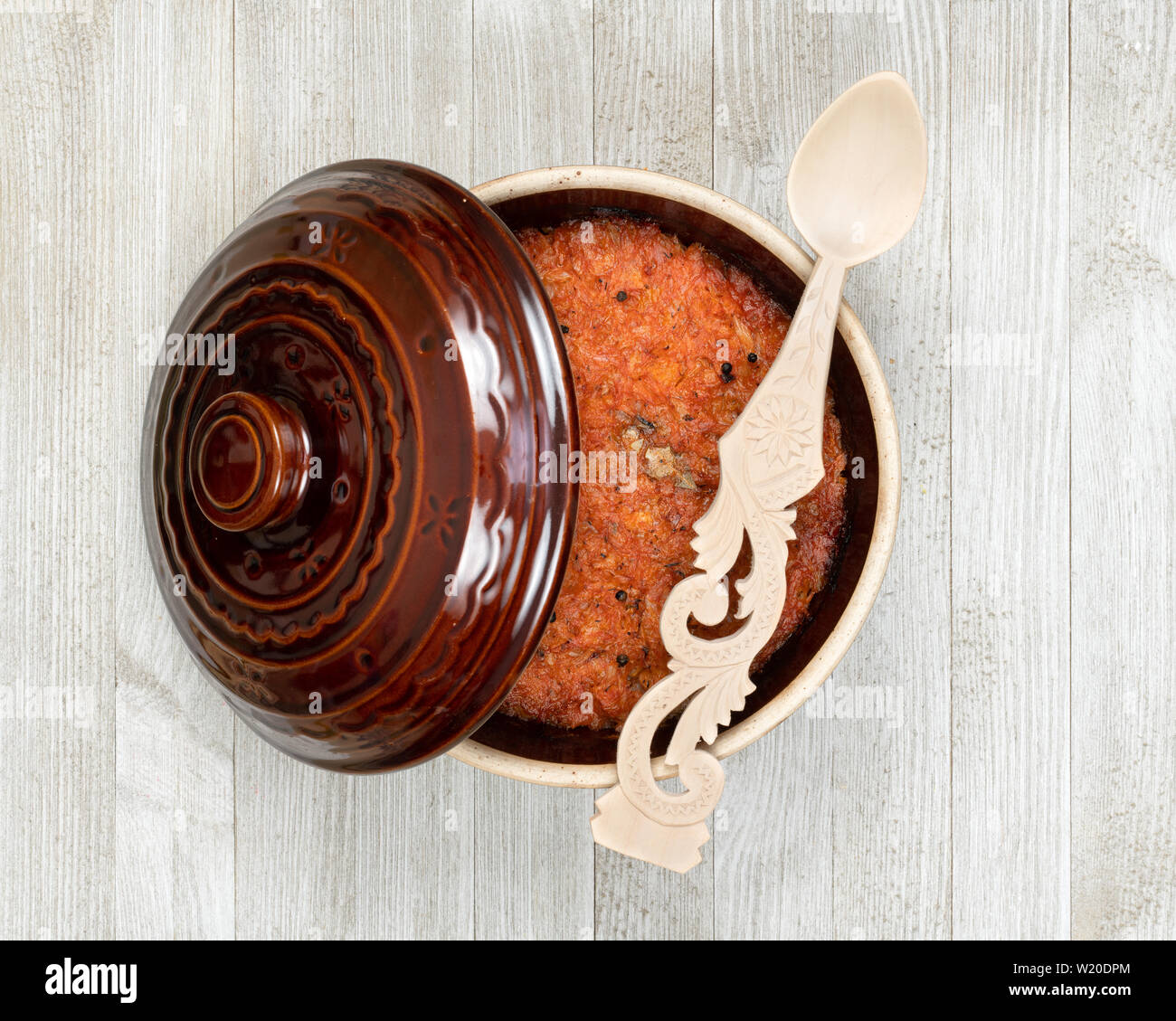 Un pot en céramique d'Europe orientale traditionnelle compote de chou et cuillère en bois décoré sur une cuisine en bois blanc. Banque D'Images