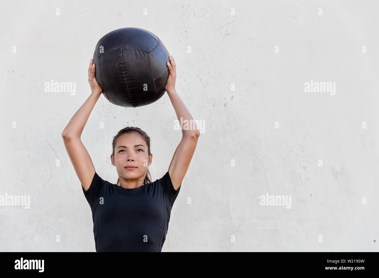 Crossfit Fitness girl holding medicine ball au-dessus de la tête pour appuyer sur l'épaule en entraînement Crossfit gym en plein air. Jeune fille asiatique fait partie supérieure du corps de l'athlète de l'exercice l'élaboration avec des boules. pondérée Banque D'Images