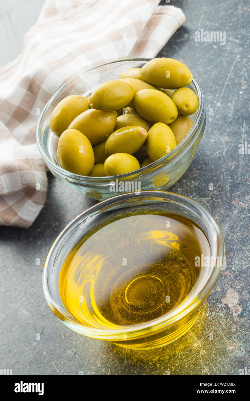 Green olives et huile d'olive dans un bol de verre sur la vieille table de cuisine. Banque D'Images