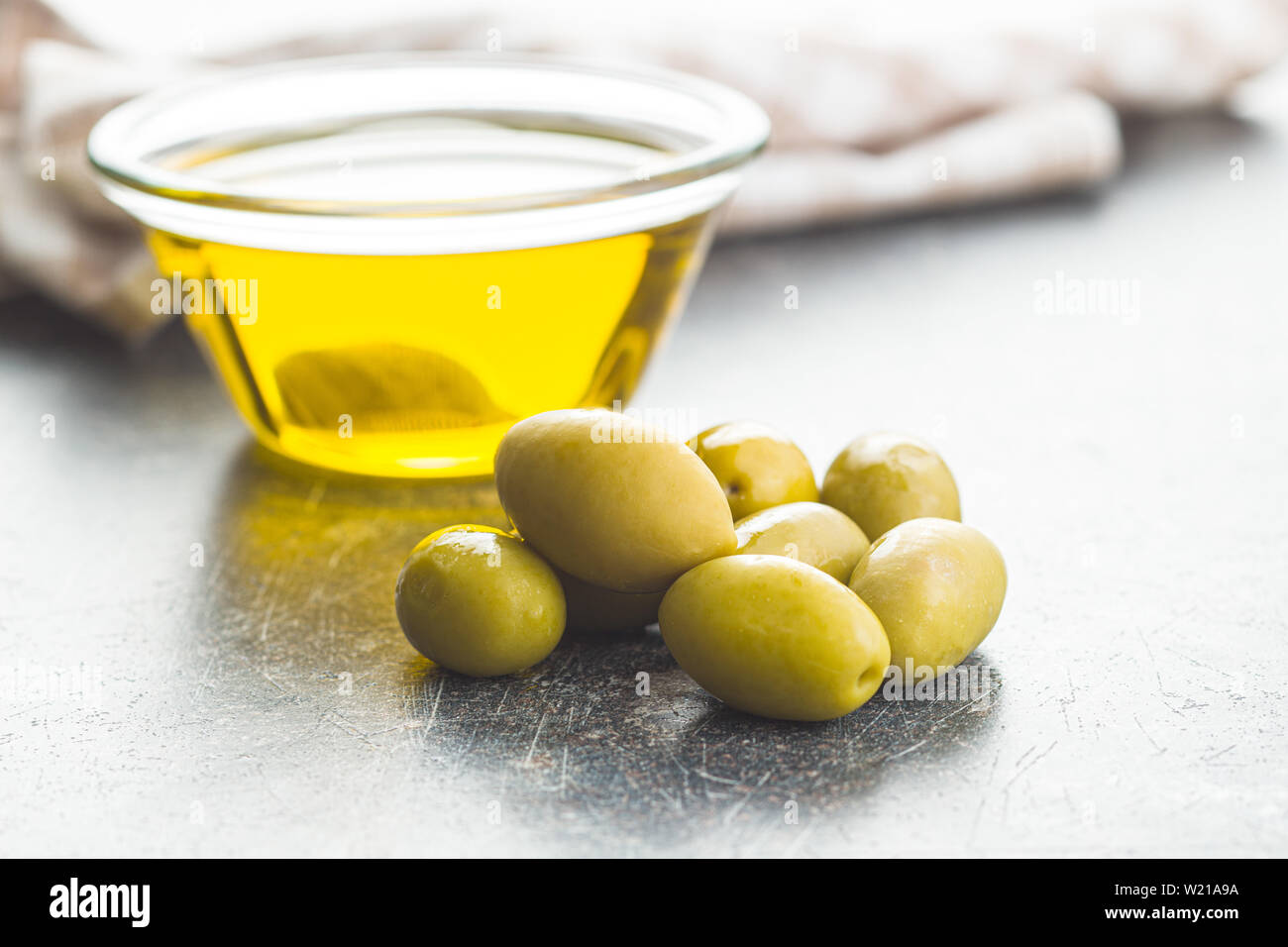 Green olives et huile d'olive dans un bol de verre sur la vieille table de cuisine. Banque D'Images