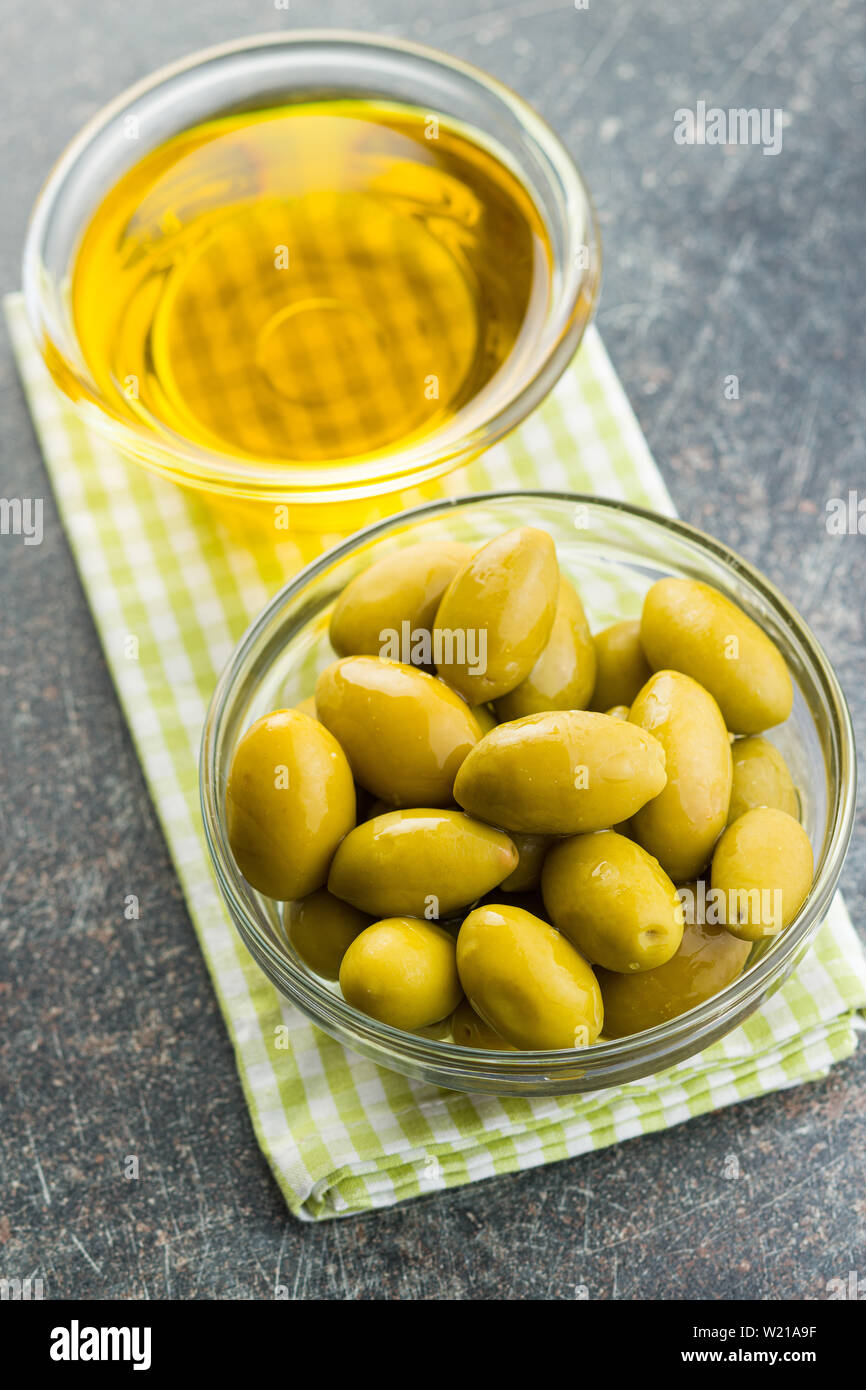 Green olives et huile d'olive dans un bol de verre sur une serviette à carreaux. Banque D'Images