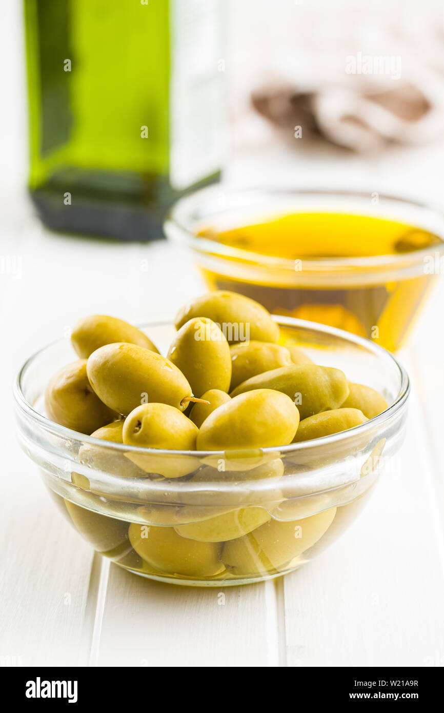 Green olives et huile d'olive dans un bol de verre sur la table blanche. Banque D'Images