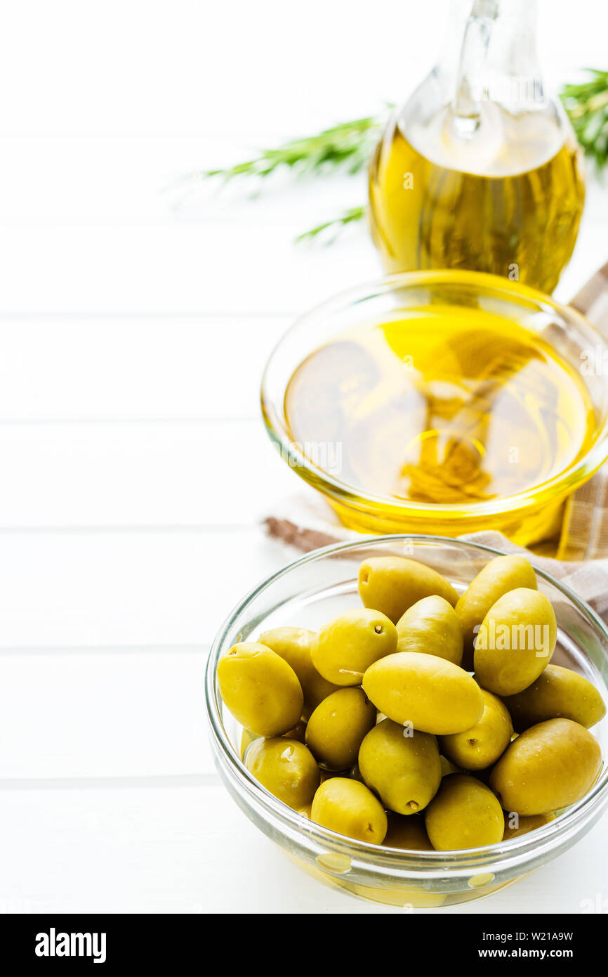 Green olives et huile d'olive dans un bol de verre sur la table blanche. Banque D'Images