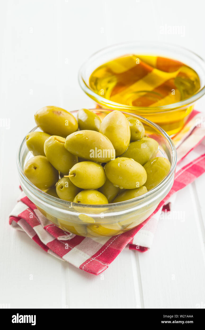 Green olives et huile d'olive dans un bol de verre sur une serviette à carreaux. Banque D'Images