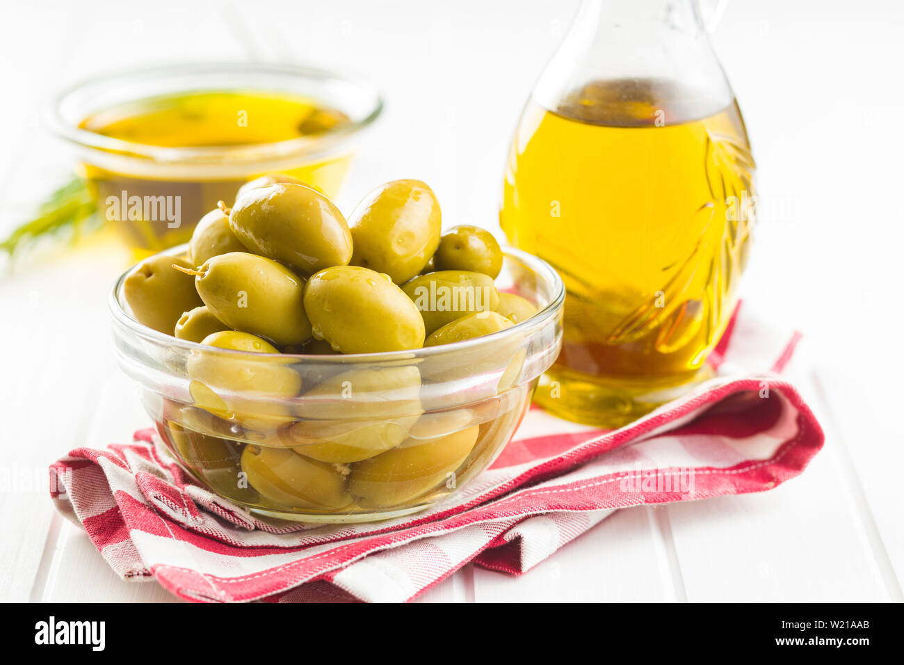 Green olives et huile d'olive dans un bol de verre sur une serviette à carreaux. Banque D'Images