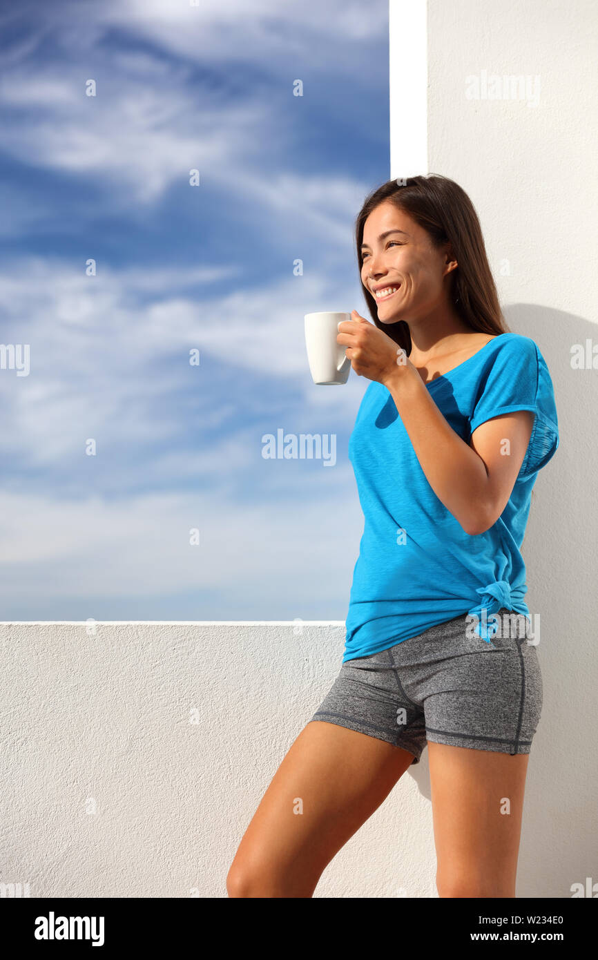 Café du matin, petit-déjeuner en yoga woman activewear à la maison piscine terrasse salon. Asian fitness fit girl drinking profiter de soleil de l'été à l'extérieur après l'exercice d'entraînement. Mode de vie sain et actif. Banque D'Images