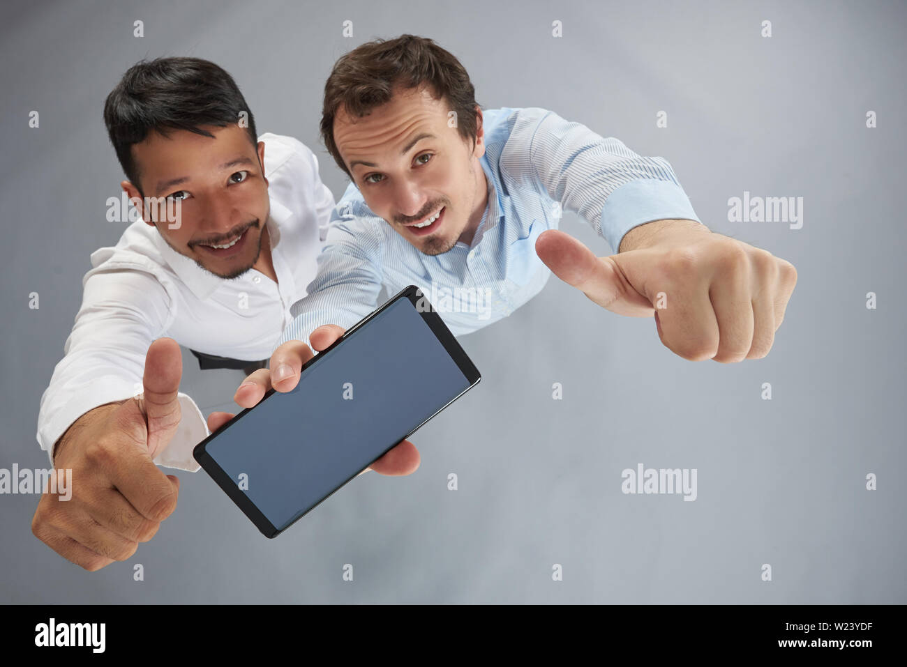 Smartphone dans jeune homme mains showing thumb up au-dessus vu de dessus en arrière-plan gris studio Banque D'Images