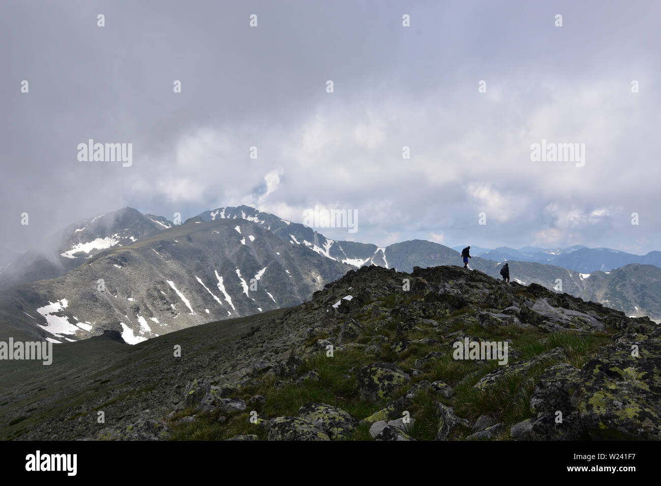 Des silhouettes lointaines de deux hommes en montagne. Temps extrême avec nuages de tempête sur Deno Peak, Rila Mountain, Bulgarie Banque D'Images