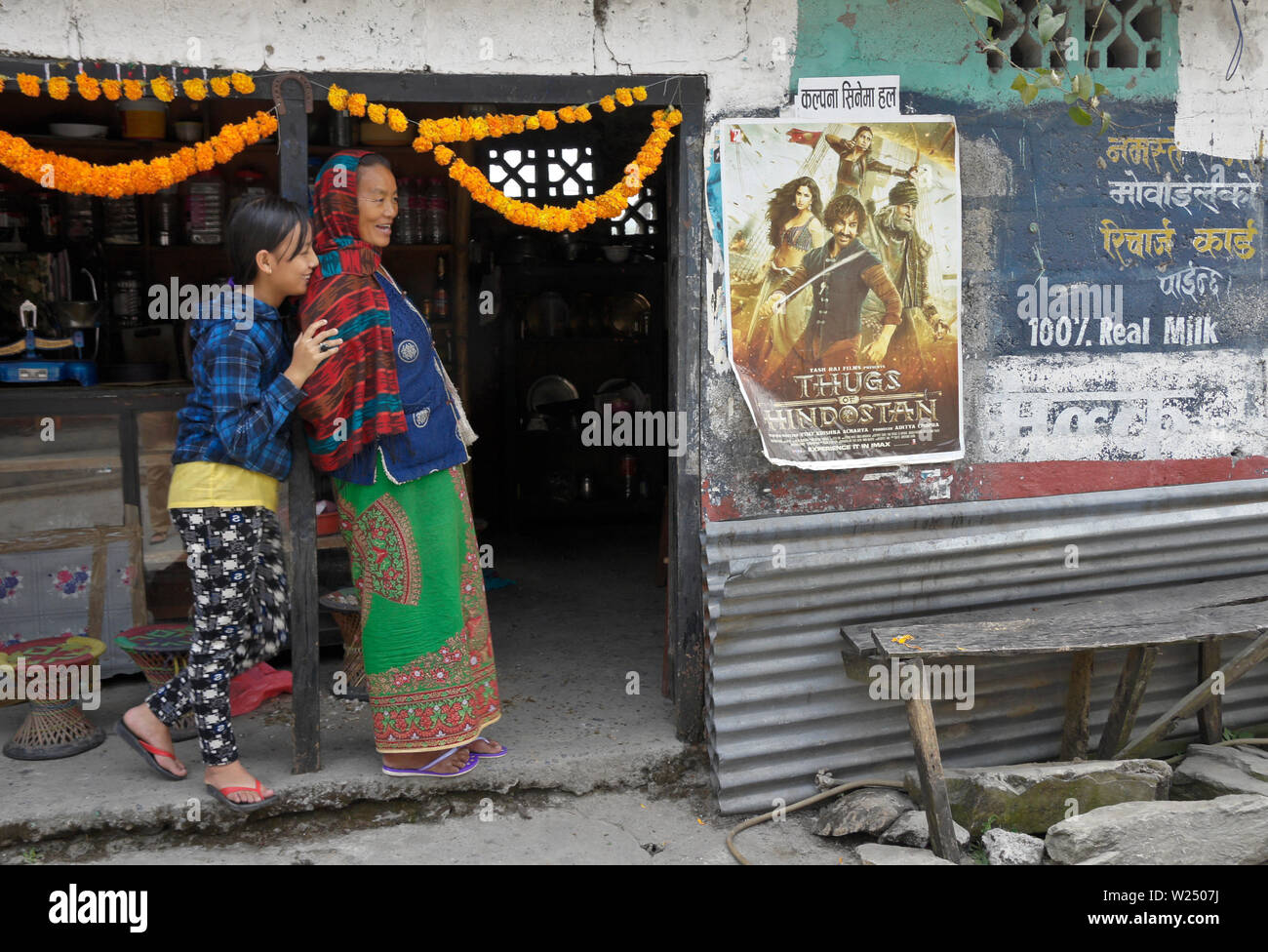 Mère tibétaine (en costume traditionnel) et sa fille (en robe) debout à côté de film affiche et annonce bilingue (anglais) et népalais, Tashi Palkh Banque D'Images