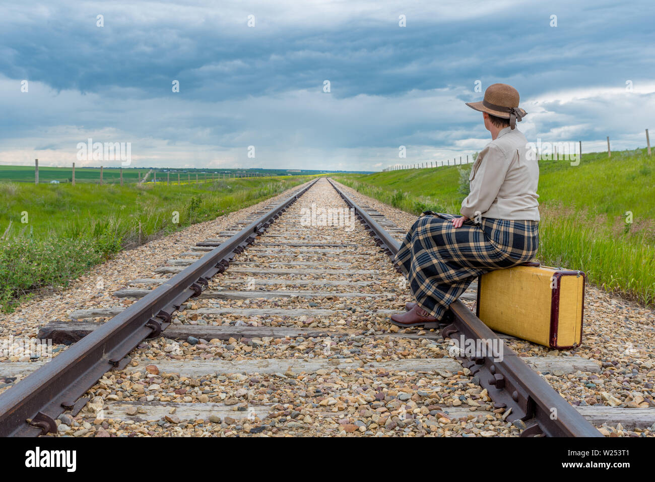 Jeune femme en robe historique assis sur vintage suitcase sur voie ferrée à la recherche vers la lumière à la fin de la ligne de chemin de fer- concept voyage Banque D'Images