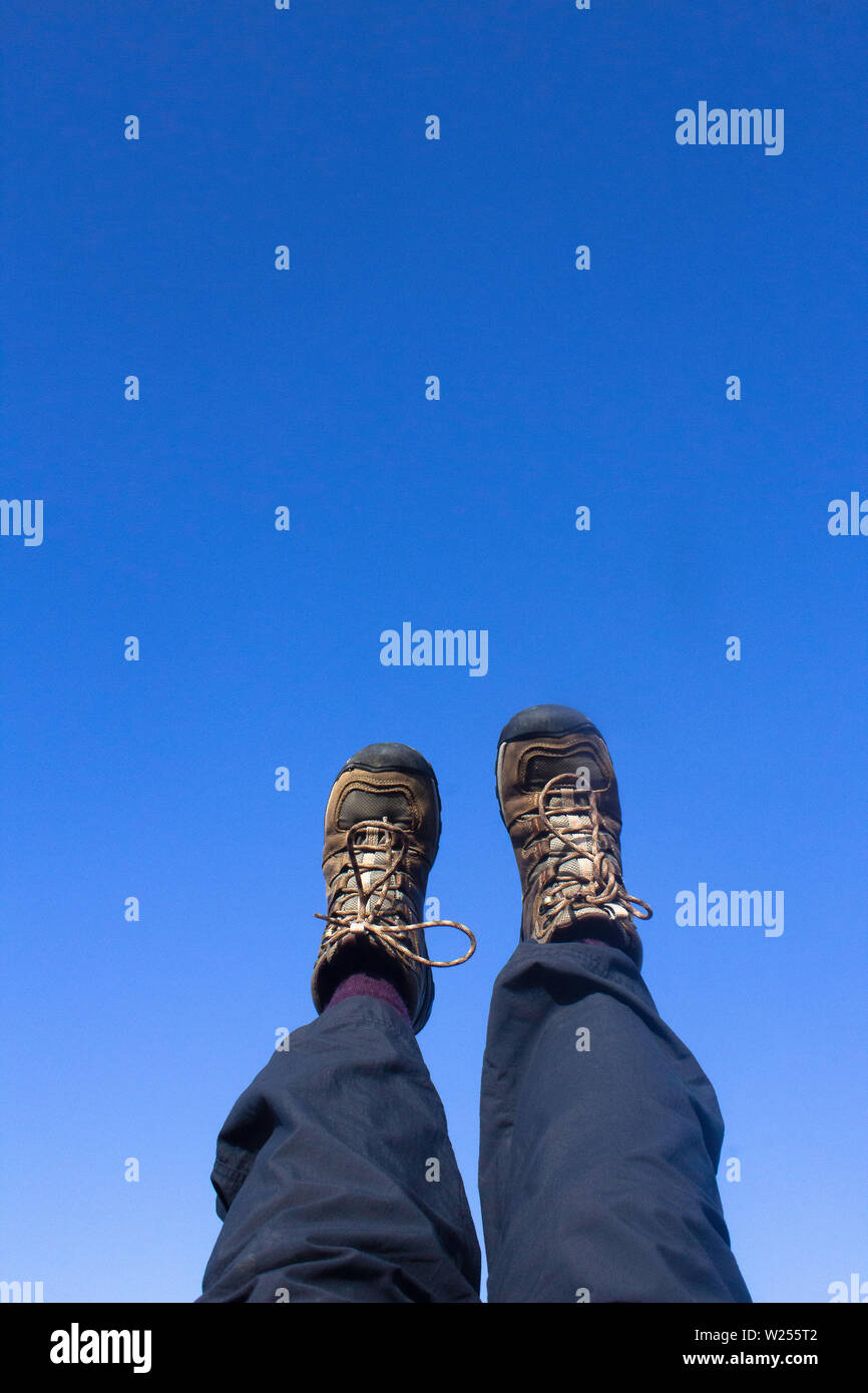 Les jambes dans des bottes de randonnée marron et bleu pantalon de randonnée contre un ciel bleu clair avec copie espace Banque D'Images