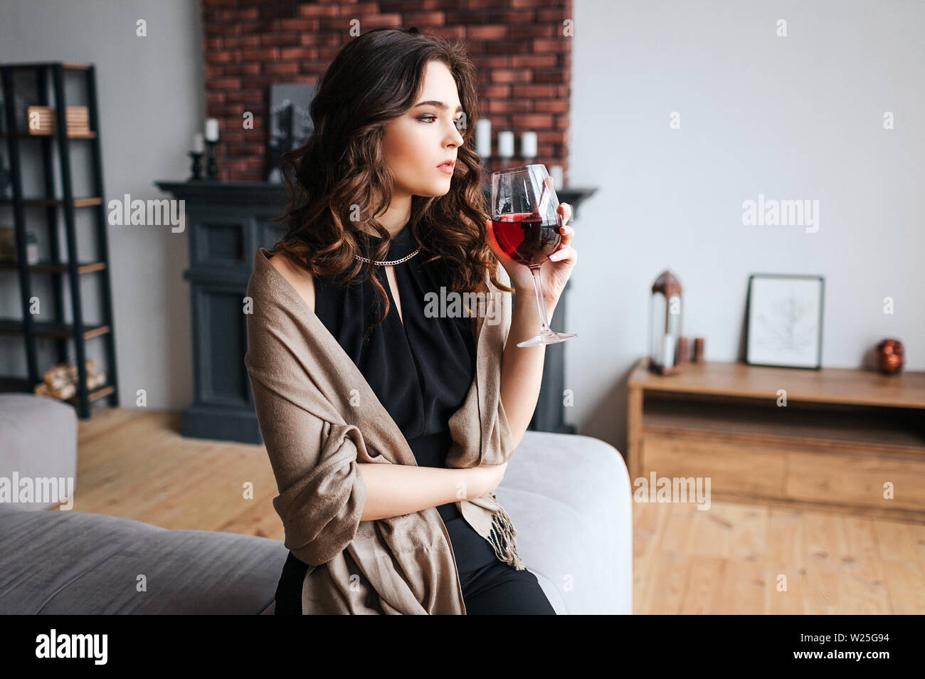 Young businesswoman travailler à la maison. Modèle calme réfléchie  maintenir le verre de vin rouge et de regarder vers l'avenir. Porter robe  sombre et marron pour homme. Seul dans la pièce Photo