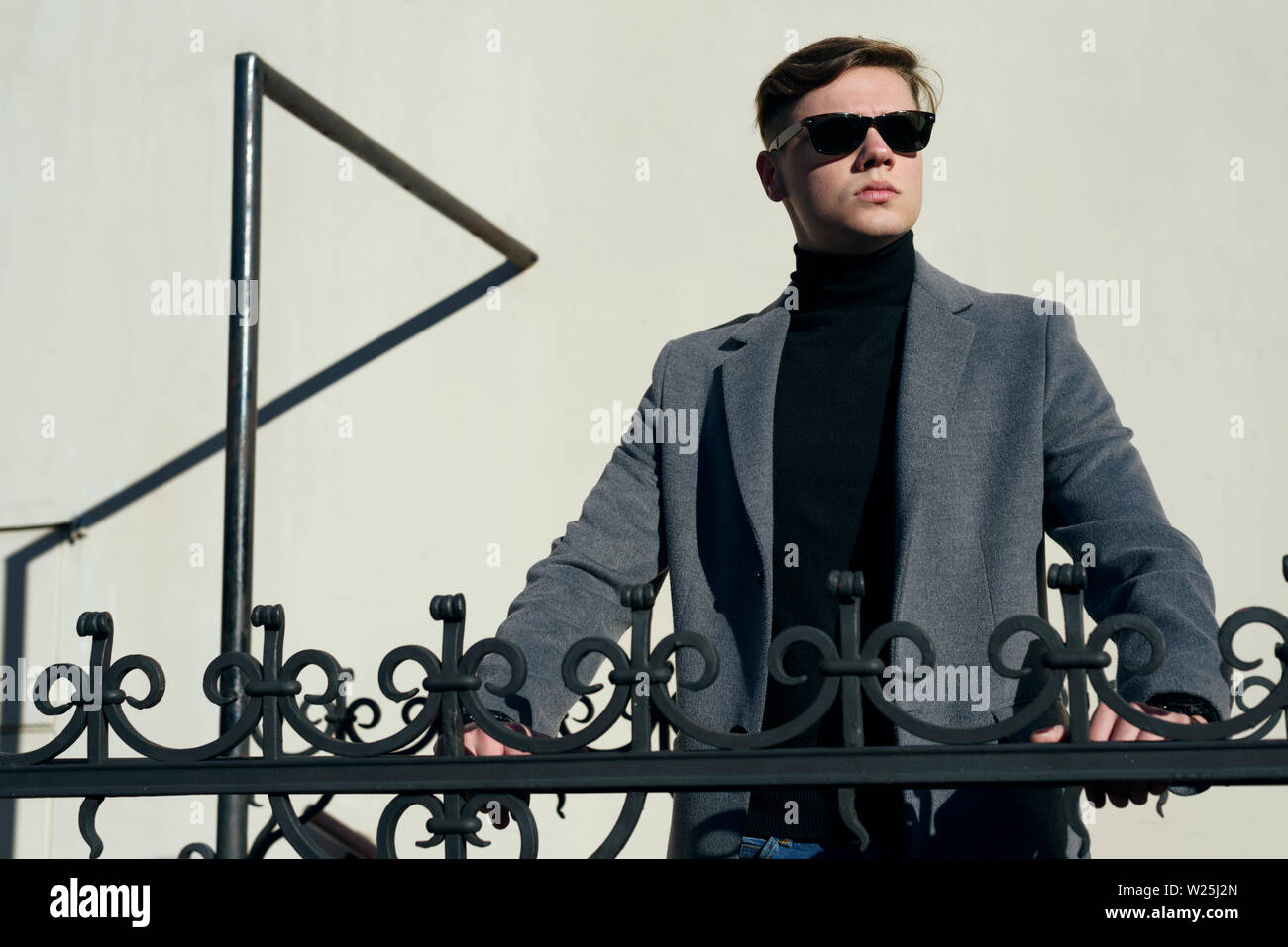 Portrait de l'homme élégant dans des lunettes de soleil, posant dans la lumière du soleil. Vêtus de col polo noir et melange veste. Décontracté élégant. Banque D'Images
