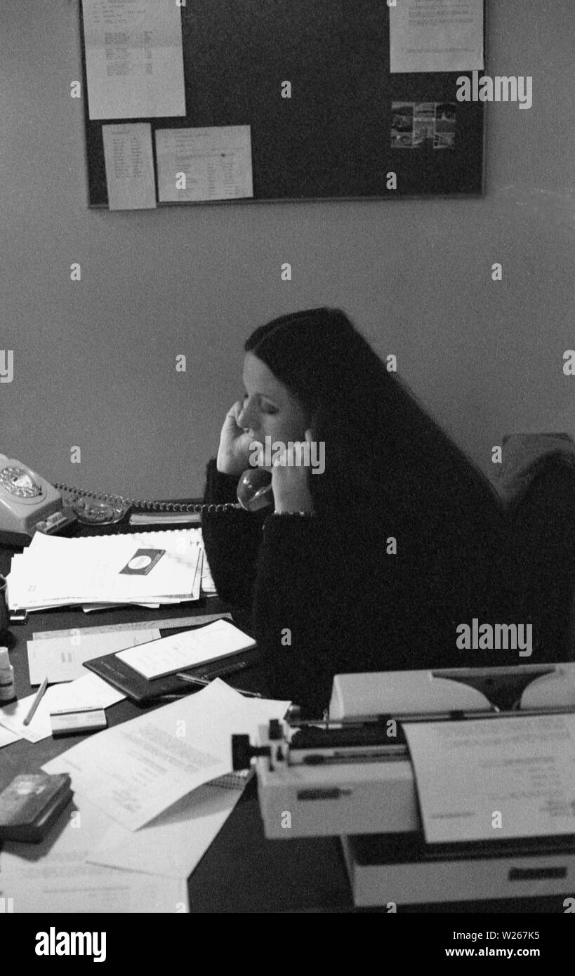 Années 1970, historiques, une jeune employée de bureau, fin des années 20 dans l'âge, parlant au téléphone, assis à un bureau, avec la paperasse et machine à écrire, en Angleterre, UK. Banque D'Images
