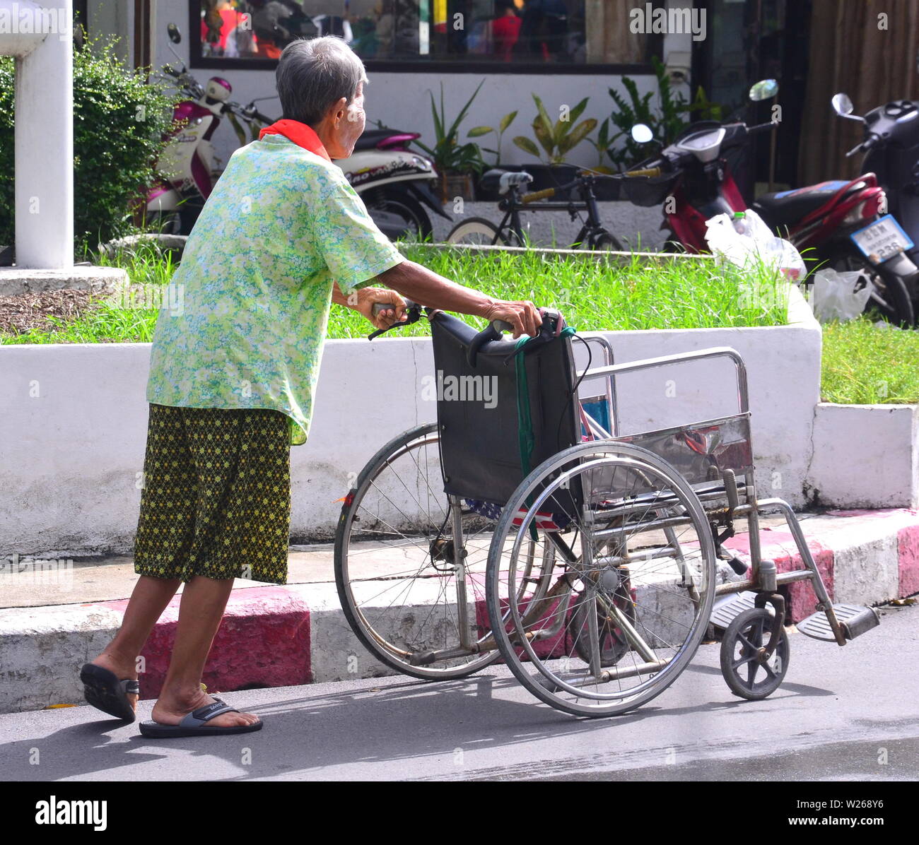 Une femme âgée pousse un fauteuil roulant, l'utilisant comme une aide à la mobilité, à Bangkok, Thaïlande Banque D'Images