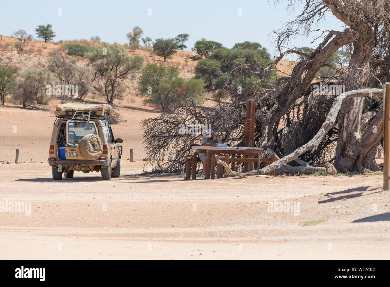 Homme ou touristiques assis à une table de pique-nique sur une aire de repos dans le parc transfrontalier de Kgalagadi en Afrique du Sud avec un véhicule 4x4 a proximité Banque D'Images